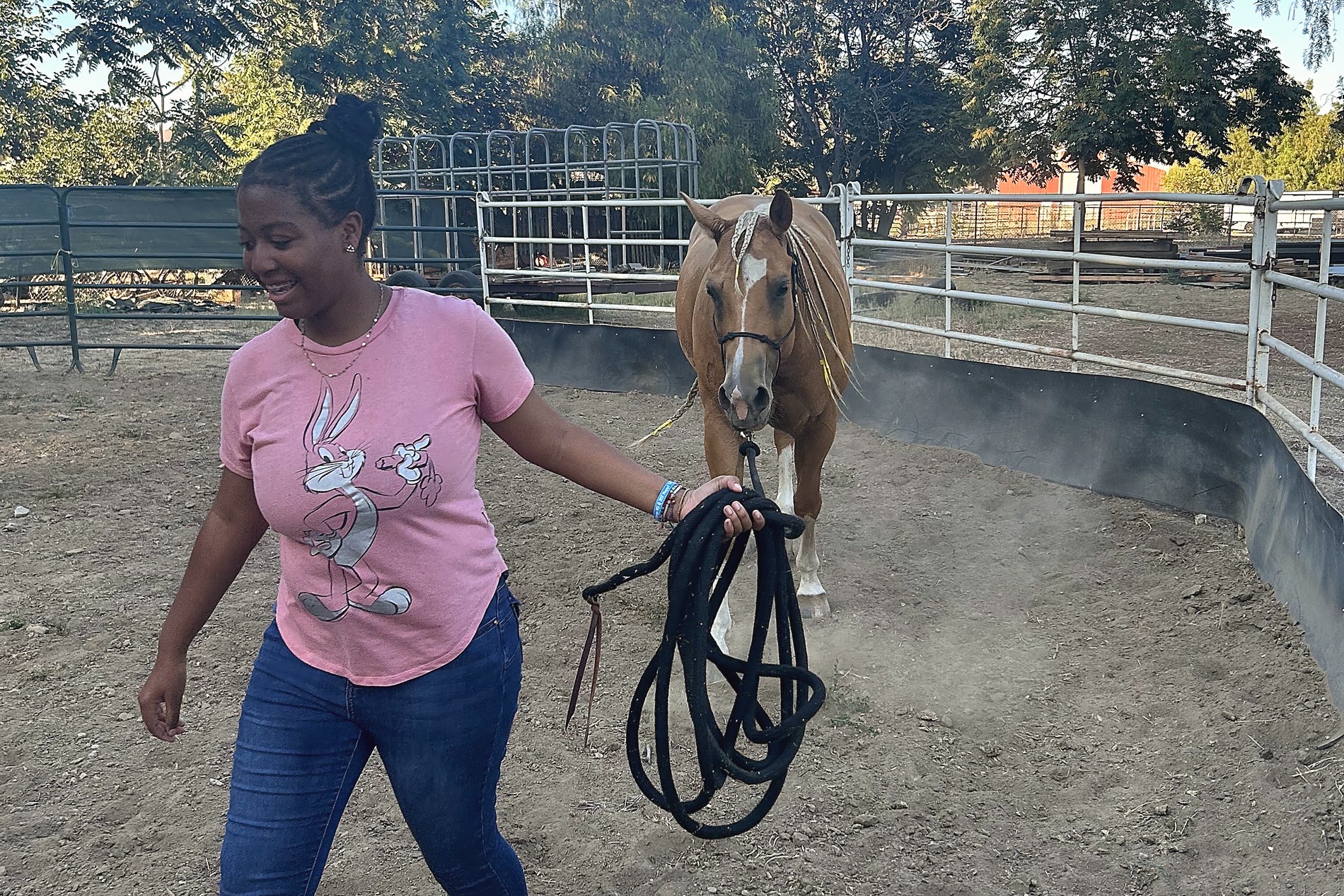 A young person leading a palomino horse by its lead rope in the round pen